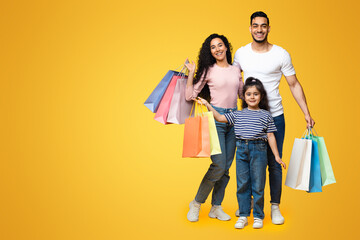 Wall Mural - Seasonal Sales. Portrait Of Happy Arab Family With Little Daughter Holding Lots Of Bright Shopping Bags, Middle Eastern Parents And Child Posing Over Yellow Background In Studio, Copy Space