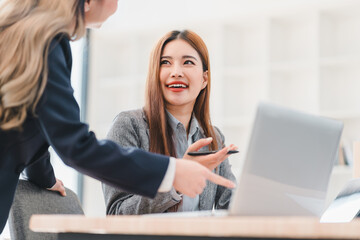 Wall Mural - Cheerful businesswoman in gray blazer discusses work with colleague while using laptop in bright modern office setting