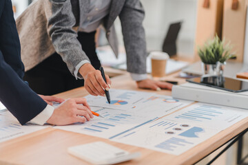 Two business professionals analyzing financial charts and graphs on wooden desk in modern office setting, discussing strategies with focus and collaboration