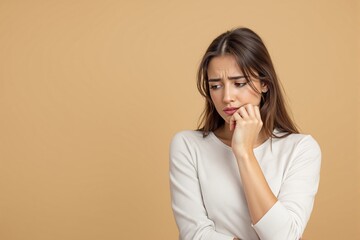 Wall Mural - Thoughtful young woman with pensive expression on light brown background.