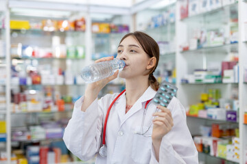 Wall Mural - woman pharmacists drinking water holding capsule blister pack at shelf stocked in pharmacy drugstore.