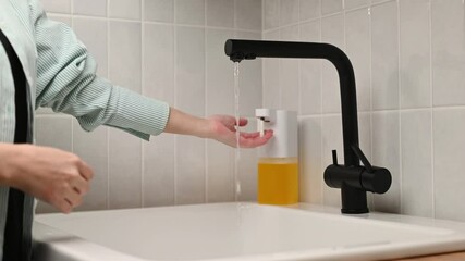 Wall Mural - An unrecognizable woman washes her hands with soap suds from a dispenser in the home room. Hand hygiene.