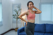 © Phimwilai - Young asian sportswoman wearing stylish sportswear, playfully touching her hair and smiling in a cozy living room, embodying a vibrant and healthy lifestyle at home