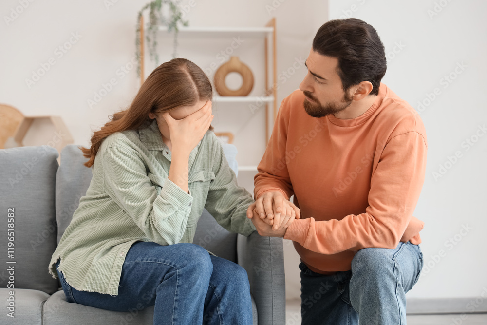 Young man apologizing to his upset wife on sofa at home