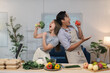 © crizzystudio - Young chefs are singing with vegetables like microphones, promoting healthy eating habits and joyful cooking in their modern kitchen, surrounded by fresh produce and takeaway boxes