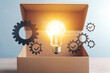 © Apaporn - A glowing light bulb emerging from an open box, symbolizing creativity and innovation with gears around it for a dynamic and inspiring concept.