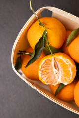 Wall Mural - Top view of whole mandarines and one peeled fruit in a wooden box on grey table background