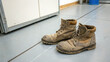 © Oksana - A pair of well-worn brown leather boots covered in dirt and grime sit on a tiled floor. The image emphasizes the hard work and resilience associated with manual labor