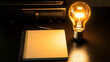 © afrah - A conceptual image of a light bulb glowing on a desk with a blank notebook and a pen
