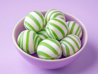 Wall Mural - Colorful striped candy balls in a small bowl on a pastel purple background, showcasing vibrant green and white swirls Ideal for sweet-themed designs and food photography