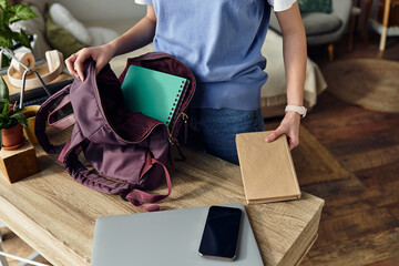 A teenage girl organizes her backpack on a stylish table in her room, embracing her day.