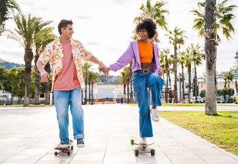 Young multiethnic modern couple with skateboards dating outdoors - Two friends having fun skating around city urban areas, concepts about youth, diversity, green trasportation and mobility