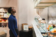© Studio Marmellata - A black man wearing a blue sweater stands near a counter in a contemporary cafe with various items on display, creating a cozy and welcoming ambiance enhanced by soft lighting and stylish decor.