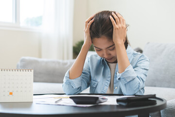 Wall Mural - Debt and financial concept, stressed asian young woman have a headache while sitting on sofa calculate expenses, income, looking bills of credit card for prepare payment or pay bills on table at home.