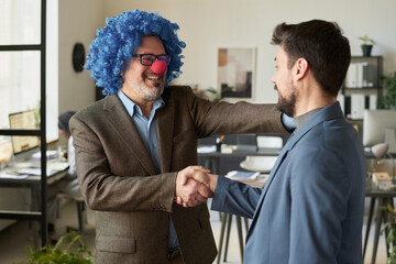 Poster - Happy mature clown man shaking hand of young employee and touching his shoulder while looking at him in coworking space