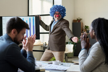 Poster - Cheerful mature boss in clown wig standing by interactive board and looking at female subordinate during presentation