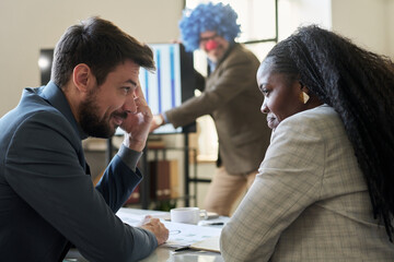 Poster - Two young smiling subordinates looking at one another while making fun of their boss wearing clown wig during presentation