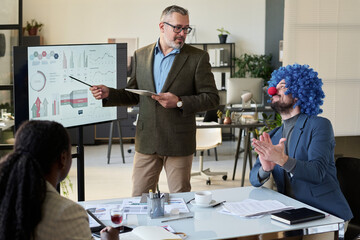 Poster - Mature male speaker pointing at interactive board and looking at clown businessman clapping hands during presentation