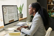 © pressmaster - Side view of young serious African American female economist looking at graphic data on computer screen and typing