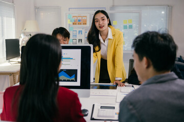 Poster - Young asian businesswoman leading a meeting, presenting charts and data analysis on a computer screen to her team in a modern office, fostering collaboration and strategic decision-making