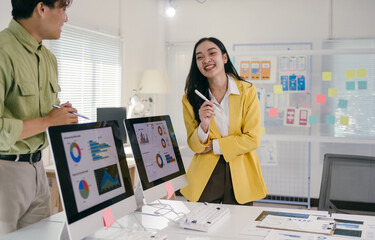 Poster - Two young professionals are discussing marketing data displayed on computer monitors, collaborating on a project in a modern office environment with charts and post-it notes on a whiteboard