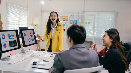 Poster - Young asian businesswoman leading a presentation in the office, pointing at computer screens showing charts and diagrams, colleagues listening and participating