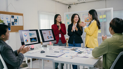 Wall Mural - Asian businesspeople clapping hands in celebration, congratulating colleagues after a successful presentation of a marketing strategy in a modern office environment