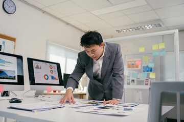 Fototapete - Young professional checking diagrams and reports on desk, using computers to develop marketing strategy, working in modern company office with glass board and post it notes