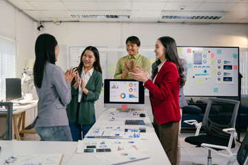 Poster - Four asian marketing professionals are clapping their hands together in the office. Celebrating a successful business project. Standing in front of a computer screen showing positive data and charts