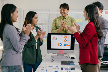 Poster - Asian marketing team clapping hands together during a meeting in the office, celebrating positive results shown on a computer screen displaying charts and diagrams