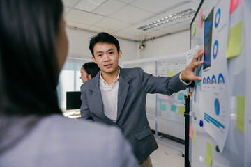 Aufkleber - Asian businessman is pointing at charts and graphs on a whiteboard while giving a presentation to his colleagues in a modern office meeting room