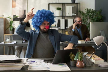 Poster - Businessman in clown wig looking at laptop screen and pressing keys while analyzing online financial data in coworking space