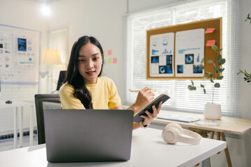 Poster - Focused asian businesswoman working in a modern office, typing on laptop and taking notes, immersed in data analysis for online meetings