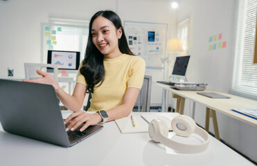 Poster - Asian businesswoman is working from home, sitting at her desk and having a video call on her laptop, she is smiling and gesturing with one hand