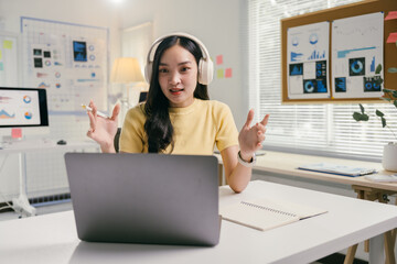 Aufkleber - Businesswoman is sitting at her desk, wearing headphones, and gesturing while speaking during a video call on her laptop