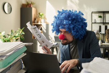 Poster - Young clown businessman with financial paper documents in hand looking at laptop screen and typing while analyzing data