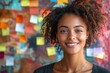 © Garik - Young woman with curly hair smiling in front of a colorful wall covered with notes in a creative workspace