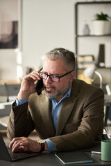 Poster - Confident mature male director of business company speaking on mobile phone and typing on laptop keypad while organizing work