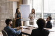 © fizkes - Two young multiethnic trainers hold corporate training event for staff, presenters making flip chart presentation, explain project details or revenue data, provide explanations. Negotiations, seminar