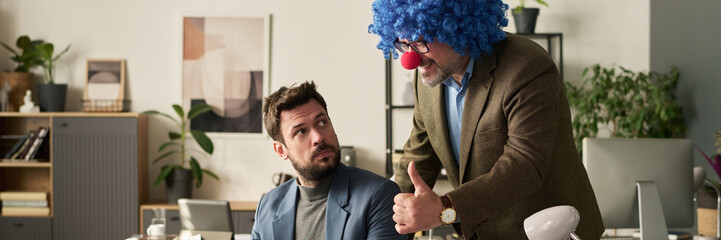 Poster - Header of happy mature male clown boss showing thumb up and looking at screen of laptop of young subordinate organizing work
