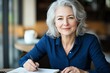 © Tondone - A confident older woman sits at a cafe table, smiling while jotting notes in a notebook