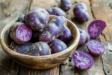 Poster - Freshly harvested purple potatoes, whole and halved, resting in a wooden bowl on a weathered wooden table