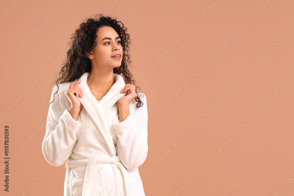 Young African-American woman in bathrobe on brown background