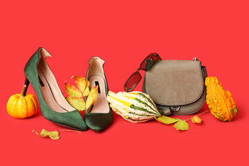 Wall Mural - Stylish high heels with green bag, sunglasses, pumpkins and autumn leaves on red background