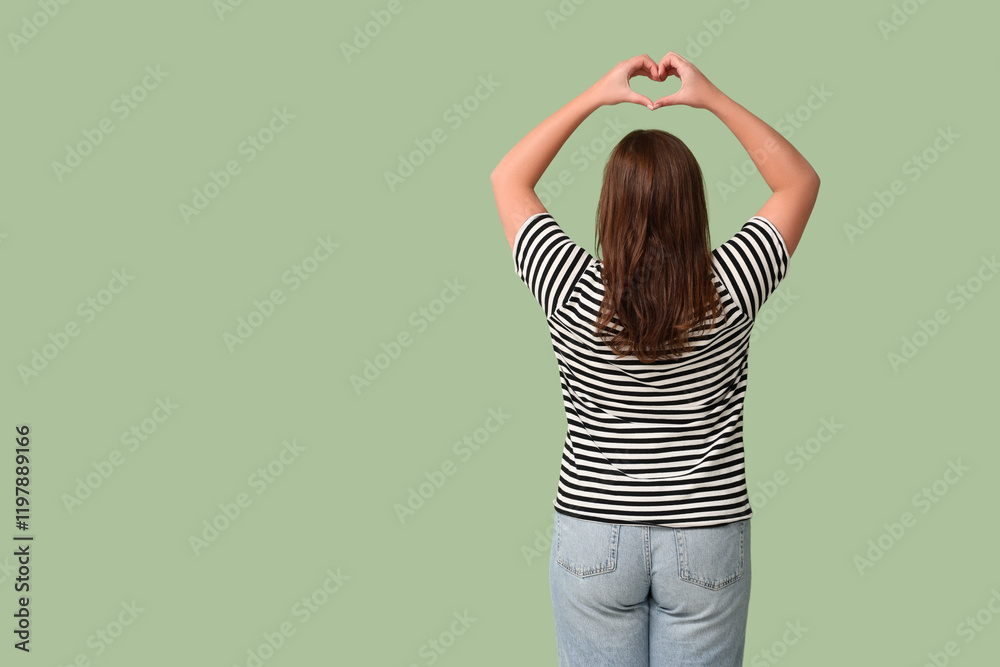 Beautiful young woman making heart gesture on green background, back view