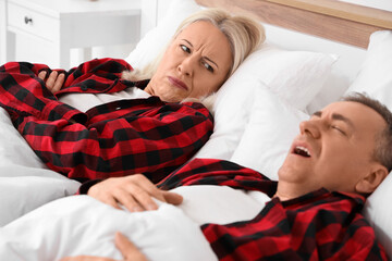 Wall Mural - Displeased mature woman lying with her snoring husband in bedroom