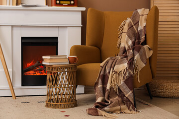 Wall Mural - Stack of books with tea cup on table and armchair near fireplace in living room