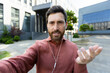 © Liubomir - Man with headphones looking into phone camera. Office worker businessman talking to colleagues and friends walking around the city using video call, smartphone app.
