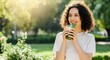 © Artiscia - Young woman with curly hair enjoys fresh green juice outdoors