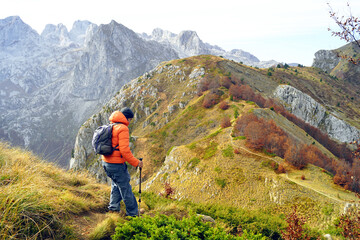 Wall Mural - Active recreation in the most beautiful places of Montenegro: a man walks along a path with a scenic view in the Prokletije National Park. A tourist carefully descends the slope using hiking poles